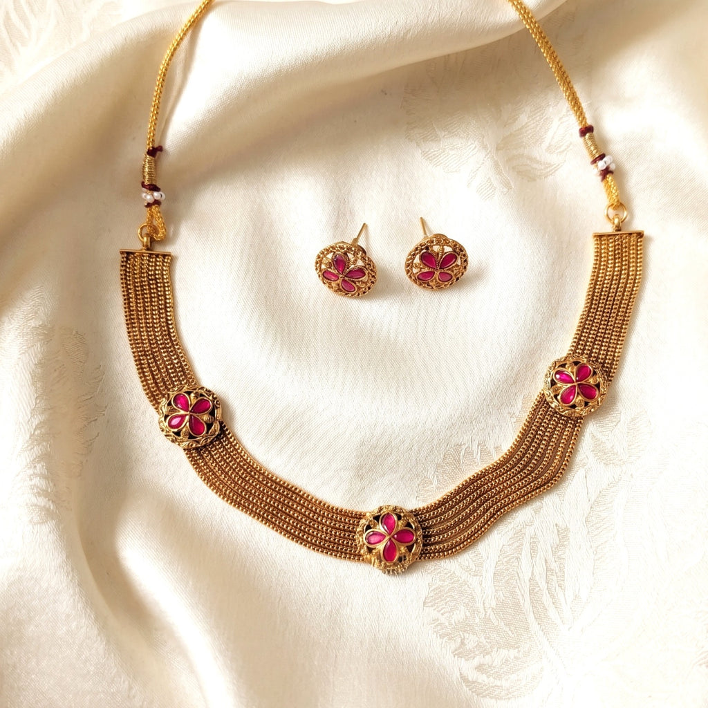 Gold necklace with pink floral designs on a white fabric background