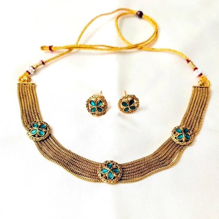 Gold necklace with green gemstones and matching earrings on a white background
