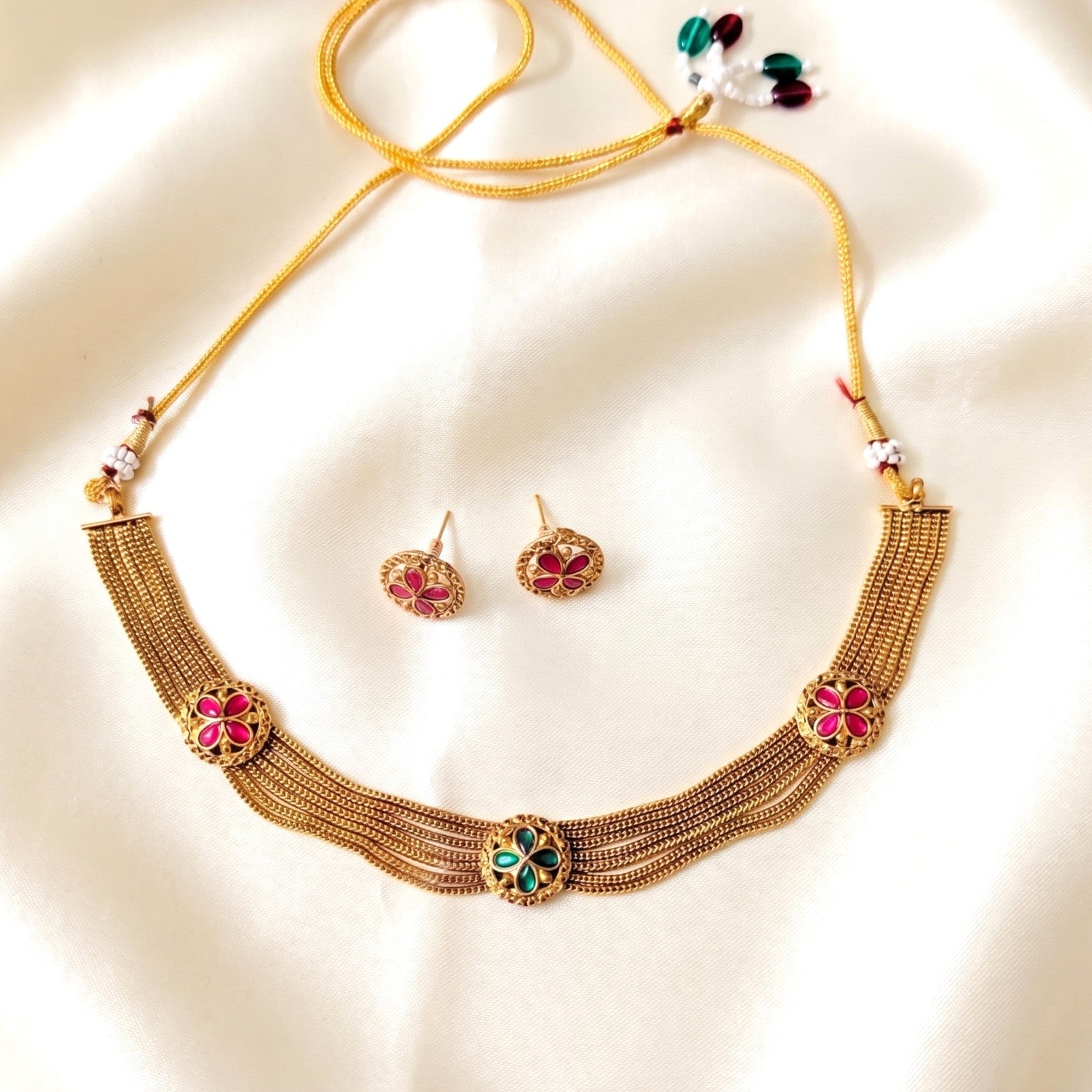 Gold necklace with floral designs and matching earrings on a beige indian jewllery background