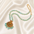 A gold-plated necklace featuring light blue-green teardrop-shaped beads and a detailed pendant with gold, green, and red accents, displayed on a draped cream satin fabric.