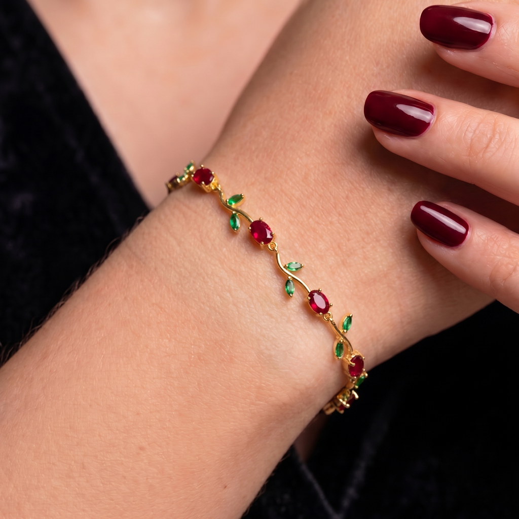 A delicate gold bracelet with red oval gemstones and small green leaf accents.