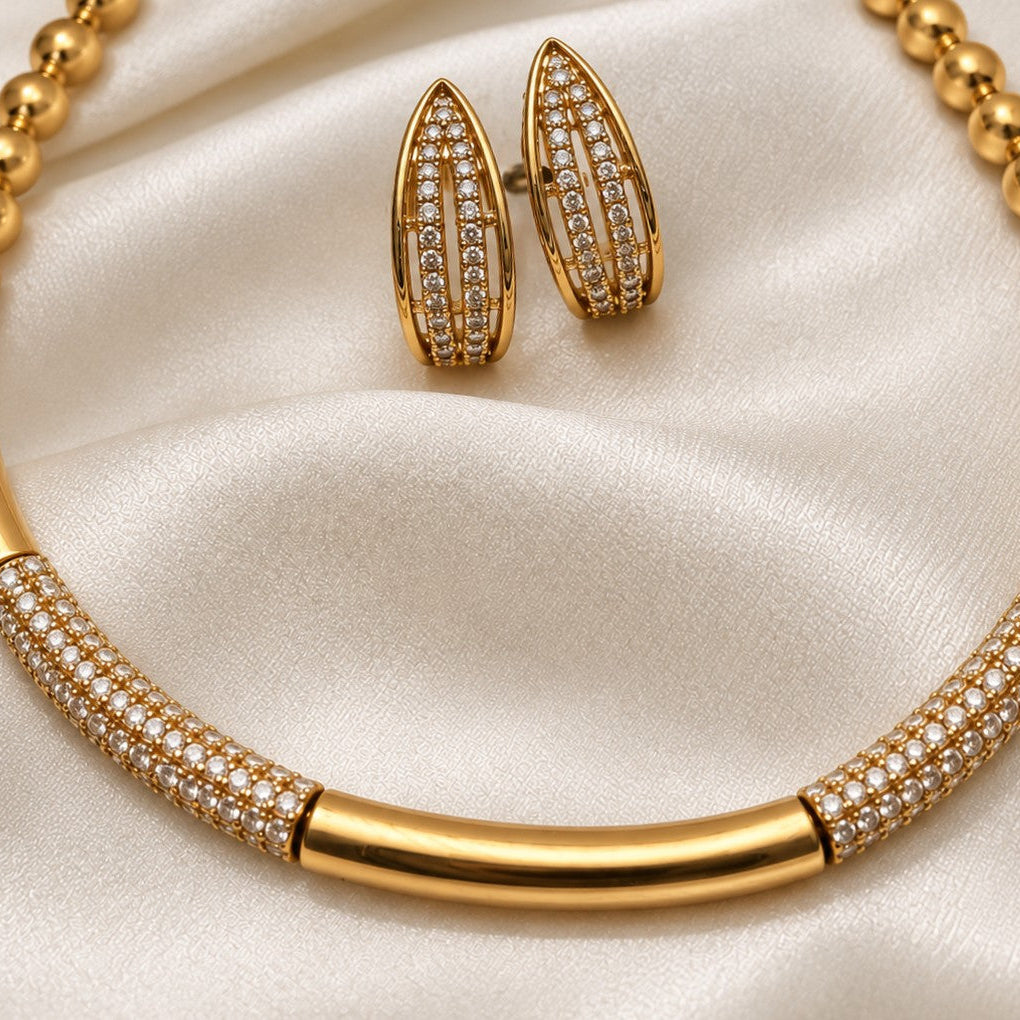 Gold jewelry set featuring a cuff hasli necklace and matching teardrop-shaped earrings, both adorned with pavé-set clear stones.
