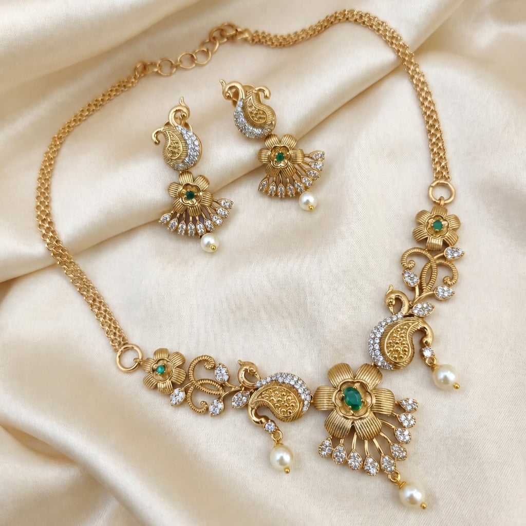Gold-plated Indian jewelry set featuring a necklace and matching earrings with green stone accents and white faux pearls
