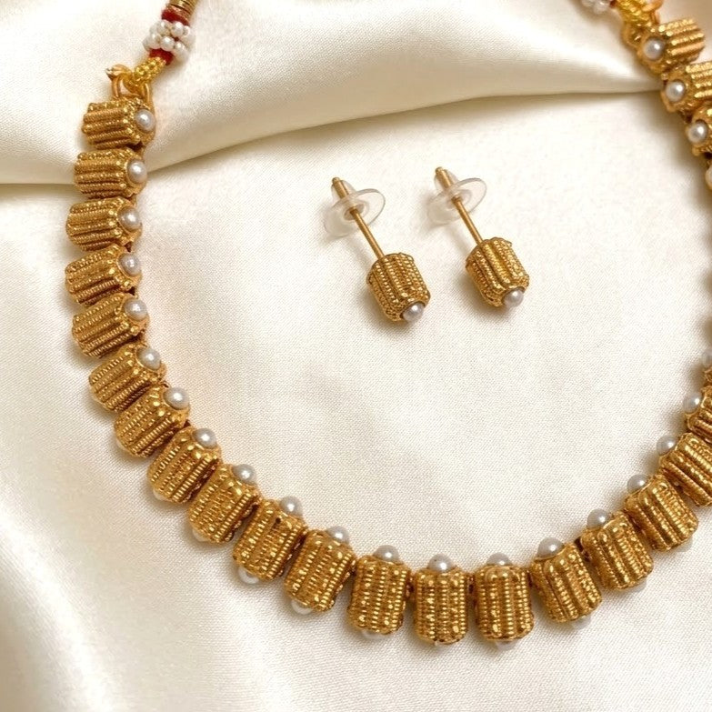 Gold beaded necklace and matching stud earrings displayed on a cream satin fabric background.