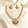 Gold-plated Indian jewelry set featuring a peacock-shaped pendant necklace and matching earrings, embellished with clear stones and small green and pink gem accents, displayed on a cream satin fabric background.