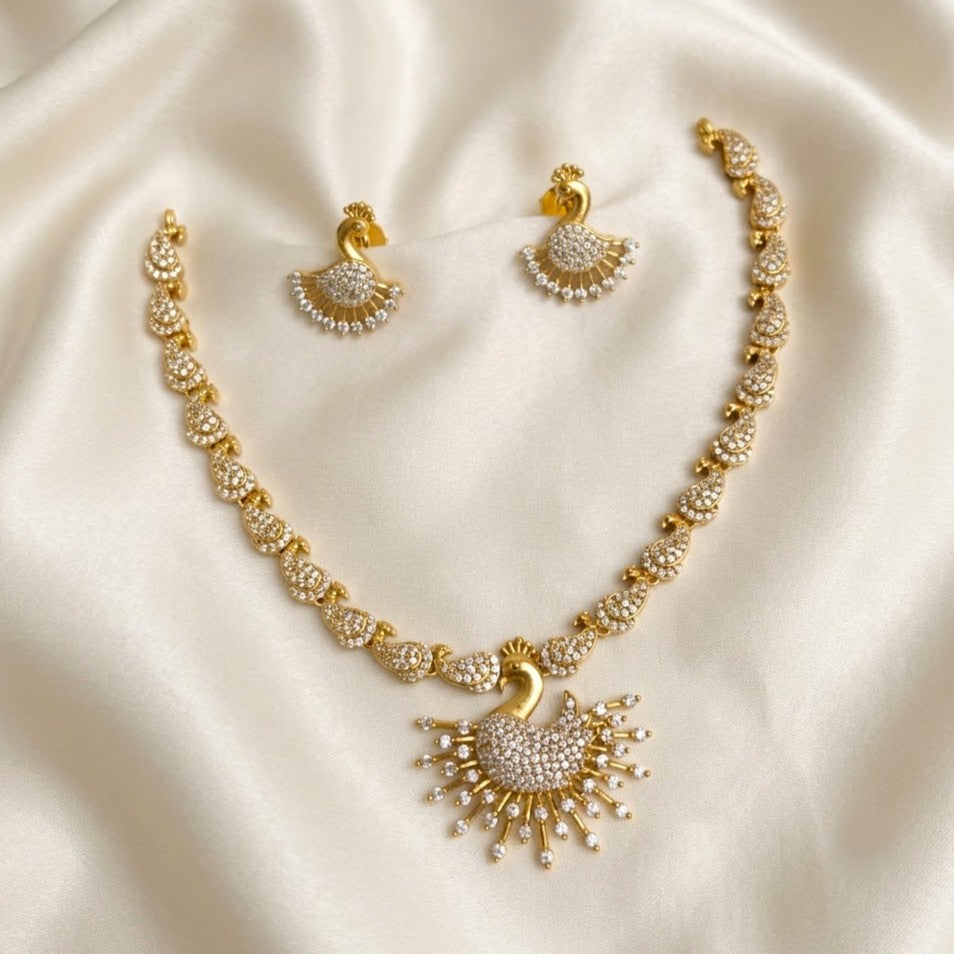 Gold and white stone jewelry set featuring a necklace and matching earrings with peacock-inspired designs, displayed on a cream satin fabric background.