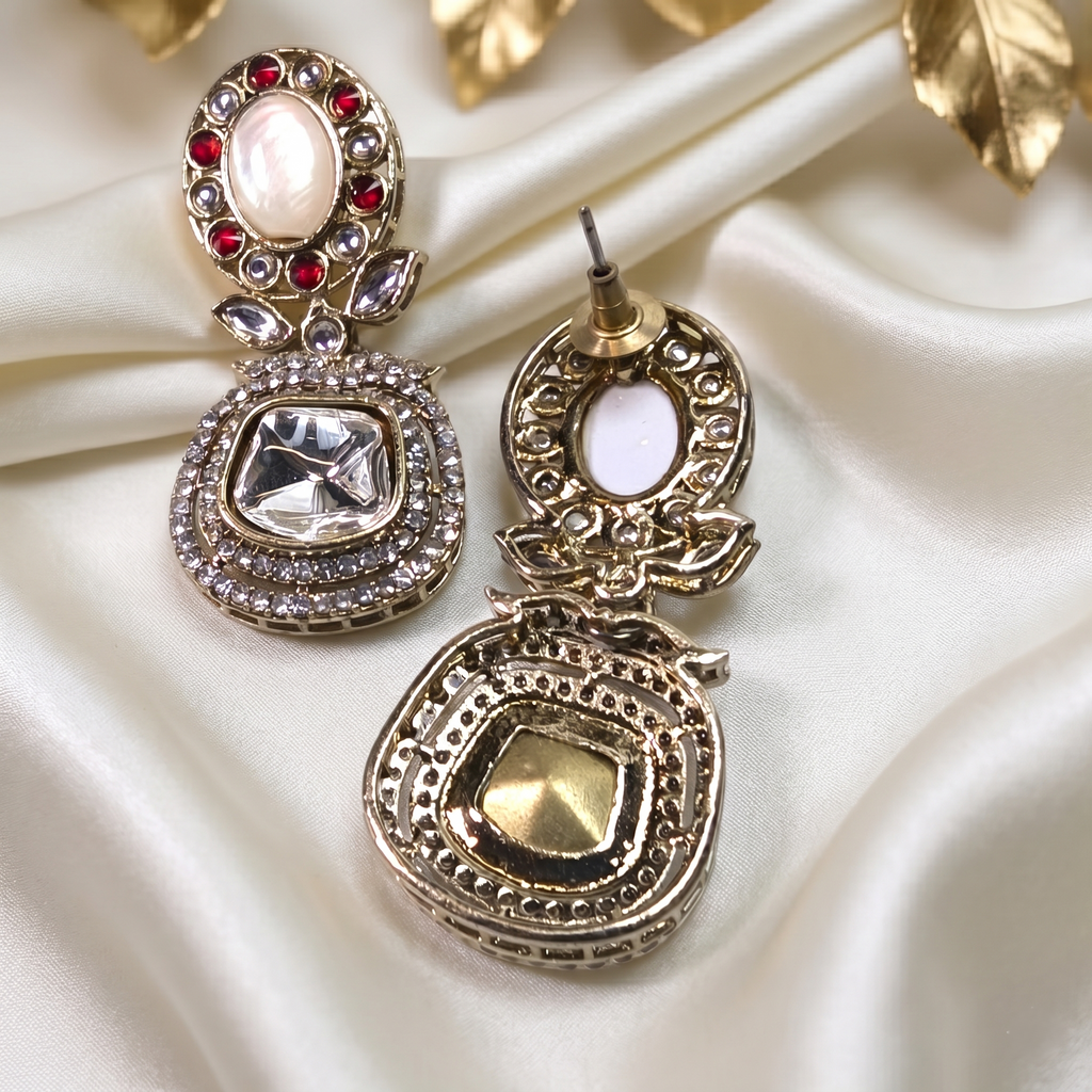 Ornate gold earrings with gemstones on a satin surface