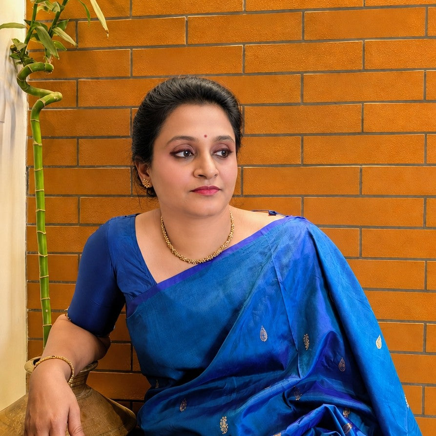 Woman in a blue saree sitting against an orange brick wall.